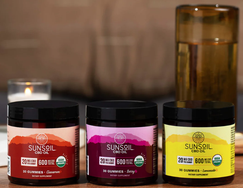 Sunsoil's cinnamon, berry, and lemonade gummy jars in a row in front of a lit white candle.