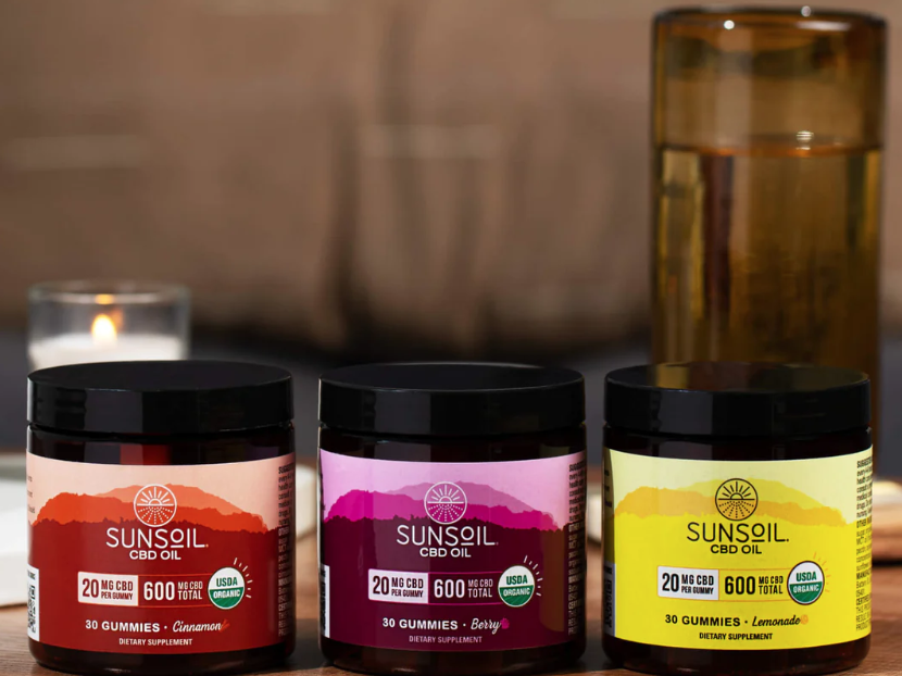 Sunsoil's cinnamon, berry, and lemonade gummy jars in a row in front of a lit white candle.